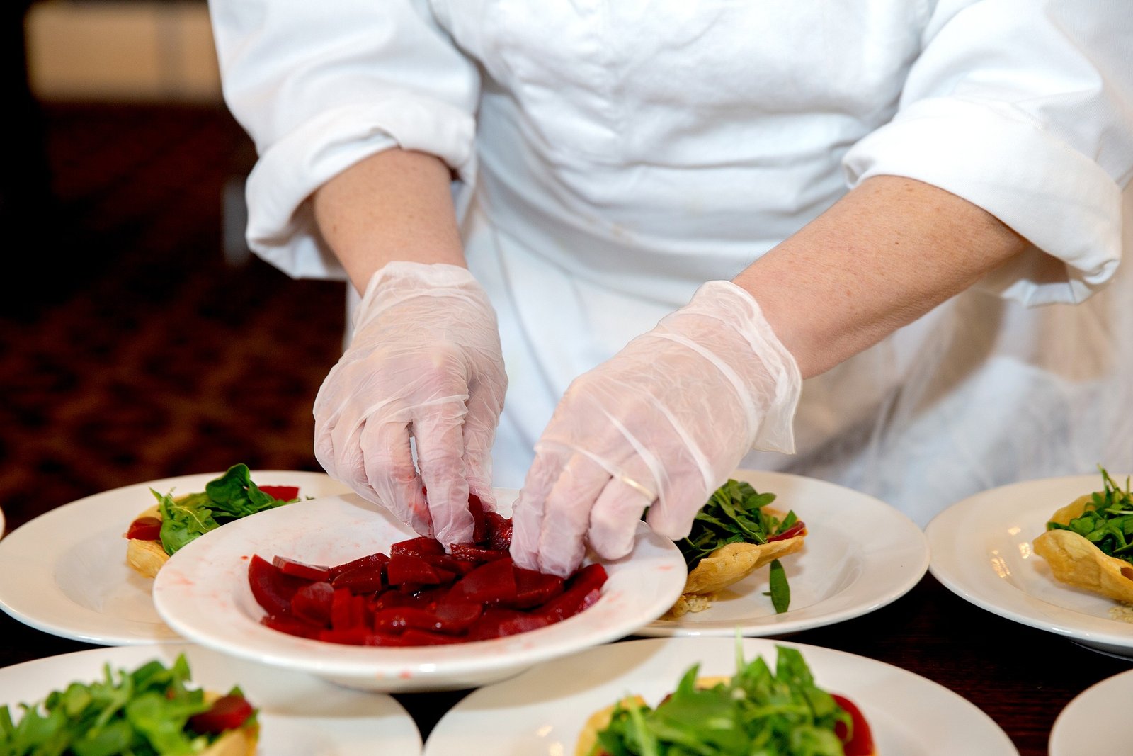 Close-up of a chef in white gloves delicately plating beetroot slices at THEA, symbolizing attention to detail and refined hospitality. Event at THEA Mackenzie Beach